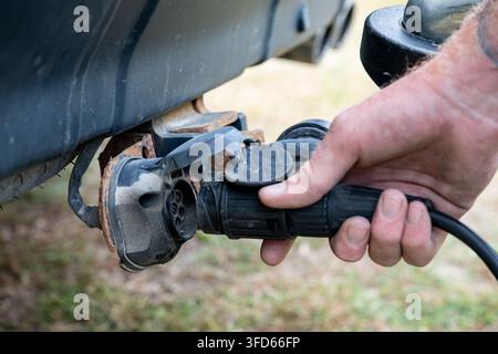 Close-up of a person connecting a trailer electrical plug to the towing vehicle socket. Practical view of trailer wiring connection and electrical hoo Stock Photo