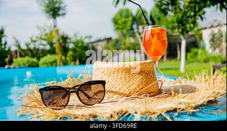 Aperol spritz cocktail with straw hat and sunglasses near swimming pool. Stock Photo
