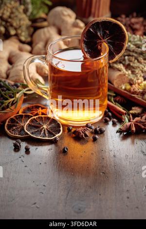 Warming herbal tea with fresh ginger, dried orange slices, juniper berries and spices served in a glass mug. Rustic composition with natural ingredien Stock Photo