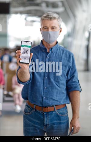 A middle-aged man with graying hair holds up his mobile phone displaying a digital health pass for travel or entry Stock Photo