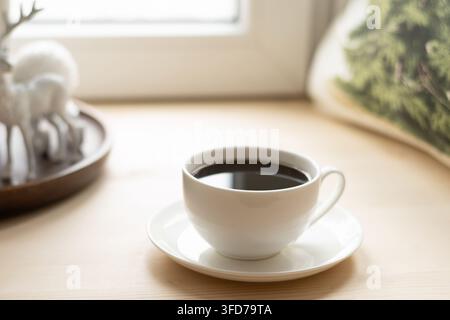 Cup of black coffee on table by window in winter. Xmas holiday Stock Photo