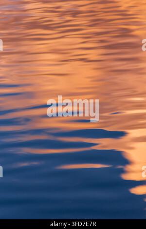 Gold sunset light reflecting on rippling blue water surface in a minimal abstract vertical composition. Stock Photo