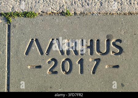 Close-up of a concrete sidewalk slab stamped with the word Aarhus, which is the second-largest city in Denmark, with small green moss growing along th Stock Photo