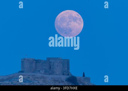 Moon glows softly above ancient stone fortress. Dark silhouette stands beneath deep blue sky. Calm, timeless scene evokes mystery and solitude. Ideal Stock Photo