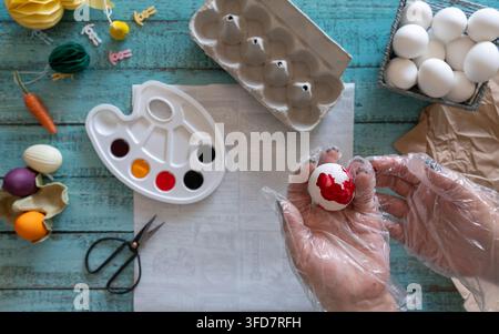 Creative flat lay of hands painting Easter eggs with watercolor paints brushes and art supplies on a rustic wooden background. Stock Photo