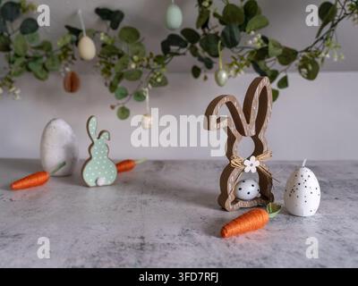 Charming Easter still life featuring a wooden bunny decoration colorful painted eggs fresh carrots and spring greenery arranged on a neutral backgroun Stock Photo