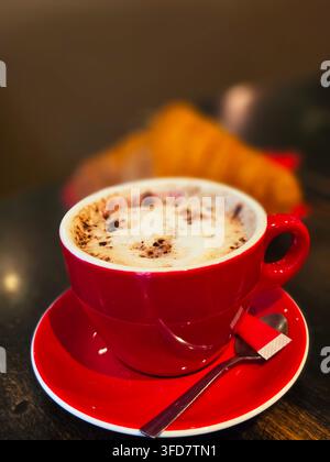 cappuccino with thick foam in a bright red ceramic cup resting on a turquoise saucer. Stock Photo