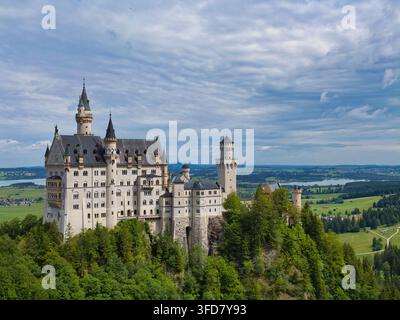 Neuschwanstein, Germany - Jul 06 2026: Neuschwanstein Castle rises above forested hills and green farmland in Neuschwanstein Germany beneath a dramatic cloud filled sky Stock Photo