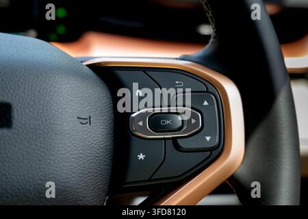 Close-up of directional navigation pad and OK selection button with copper trim on a leather steering wheel inside a modern car cabin. Stock Photo