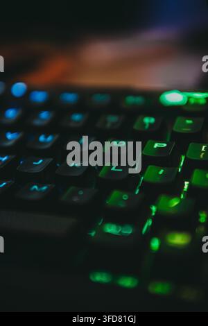 A macro shot captures the glowing blue and green backlit keys of a mechanical gaming keyboard in a dimly lit room. Stock Photo