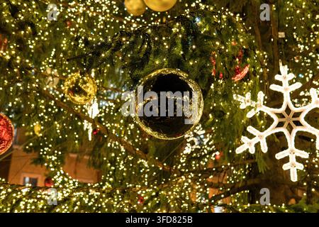 A large red bauble hangs beside a smaller gold ornament, framed by glowing string lights on a decorated tree. Stock Photo