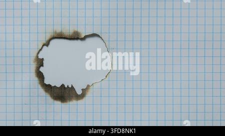 Graph paper showing a burnt hole with charred and scorched edges on a white background Stock Photo