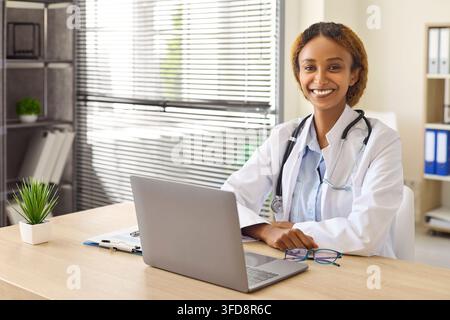 Smiling Female Doctor Working on Laptop in Bright Medical Clinic Office Portrait Stock Photo