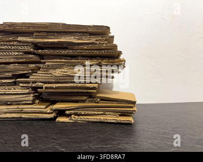 Stack of used cardboard boxes sits on a black surface against a plain white wall Stock Photo