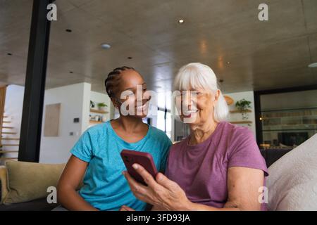 Senior woman and African-American woman in purple and teal tees holding red phone smiling at home Stock Photo