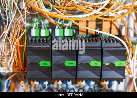 A detailed view of a messy electrical control panel featuring numerous wires, relays, and programmable logic controller modules Stock Photo