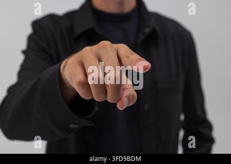 Man in a black shirt pointing his index finger forward at the camera against a neutral background. Concept for touching a modern digital screen, selec Stock Photo
