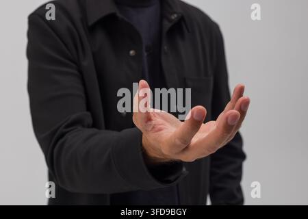 Close-up of a man in a black shirt holding an open cupped hand out against a plain background. Ideal concept for displaying virtual holograms, product Stock Photo