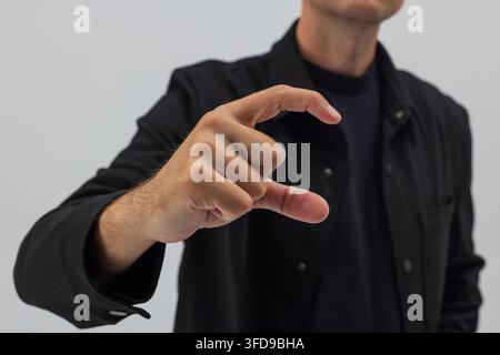 Close-up of a man in a black shirt holding hand in a C-shape gesture. Concept for holding invisible small object, measuring size, or interacting with Stock Photo