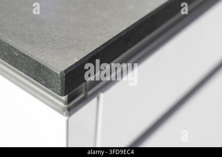A close-up view highlights the sophisticated detail of a dark stone countertop edge, complemented by polished metal supports and a clean white backgro Stock Photo