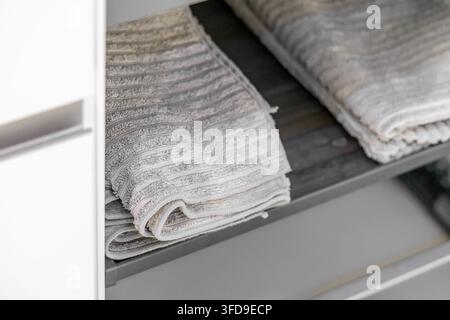 Close-up view of soft, textured grey towels arranged on a shelf, suggesting organization and comfort in a home or hotel setting Stock Photo