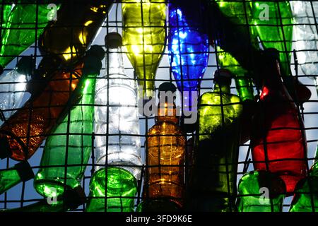 Numerous recycled glass bottles of various shapes and sizes are intertwined within a dark metal grid, illuminated from behind by daylight, casting vib Stock Photo
