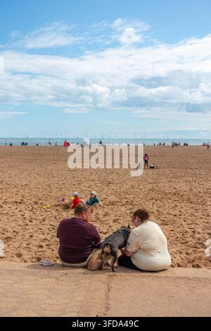 A couple sit with their dogs on the edge of the promenade wall at the top of Skegness beach in Lincolnshire, UK Stock Photo