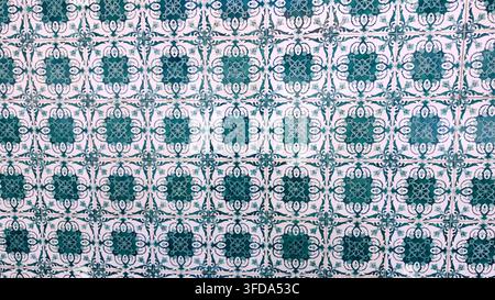 This high-angle shot showcases a wall of glazed ceramic tiles featuring intricate teal and emerald green floral patterns. The aged white background di Stock Photo