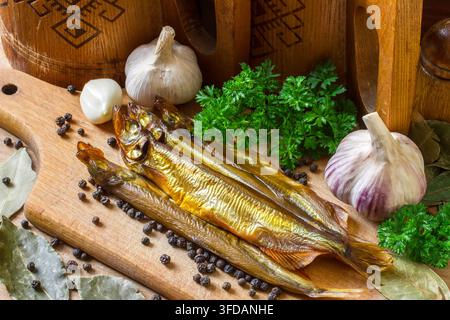Composition with smoked fish capelin with spices and kitchen utensils. Smoked capelin on a wooden cutting board. Stock Photo