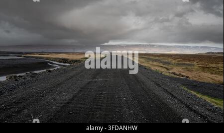F249 empty gravel road winding through a wide, desolate plain under heavy, dramatic storm clouds in Iceland. Icelandic landscape. Storm stormy sky Stock Photo