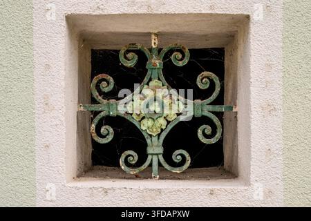 This close-up features an ornate green iron grate on a textured wall. Adorned with a floral motif and cobwebs, the weathered metal fixture serves as b Stock Photo