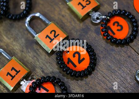 A numbered padlock and key tags on dark wooden surface creating organized security concept with vivid orange labels, black bead rings, and metallic ha Stock Photo
