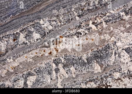 Close up of a polished granite slab showing diagonal white and grey mineral banding with rust brown inclusions, a natural stone texture used for Stock Photo