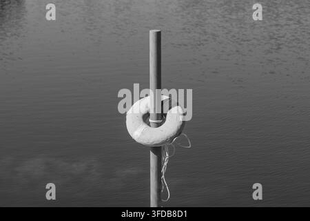 An abstract, tranquil scene featuring a simple lifebuoy secured by a rope against the backdrop of calm water and sunlight. Stock Photo