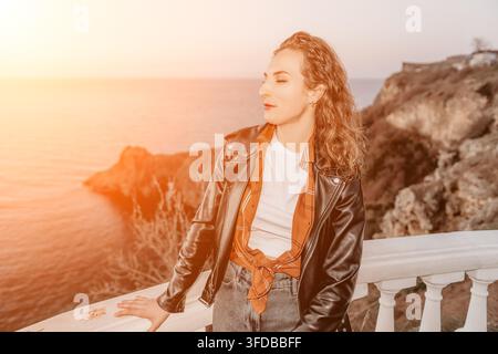 Woman sunset terrace young woman in a leather jacket enjoying the coastal breeze on a white stone balcony at dusk Stock Photo