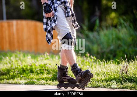 Young person with protective gear roller skating on paved trail outdoors during summer daylight Stock Photo