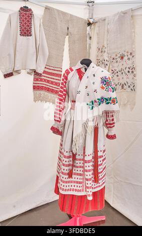 Authentic female Belarusian national costume on mannequin, featuring embroidered linen shirt, woven striped skirt, apron, belt, and floral shawl from Stock Photo