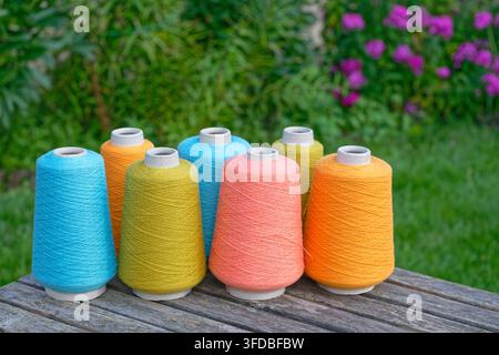 Large spools of colored industrial thread organized in rows on natural background Stock Photo