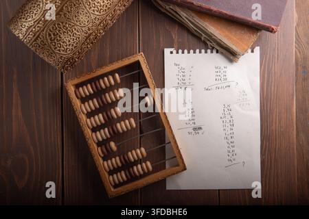 Wooden abacus beside handwritten calculations and old books on a rustic wooden table Stock Photo