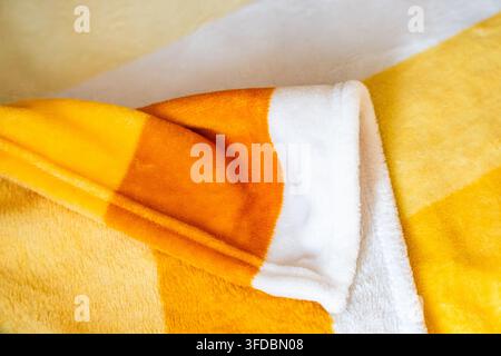 Close up of a folded soft yellow plaid fleece blanket highlighting fluffy texture, comfortable warmth, and vibrant home interior decor styling. Stock Photo