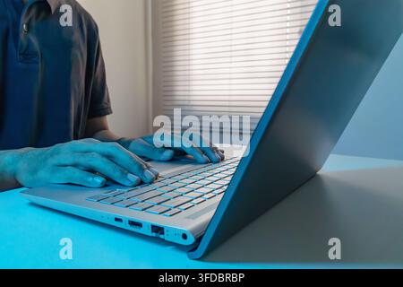 A man working on a laptop in a room with blue ambient lighting Stock Photo