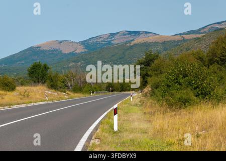 Curving rural mountain road leading through sunny green summer landscape Stock Photo