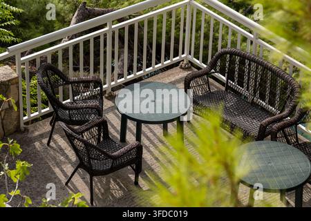 Empty wicker patio seating area with round tables on sunny terrace Stock Photo