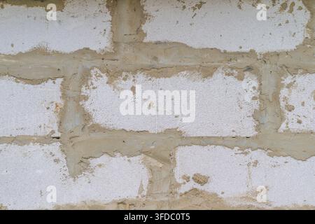 Detailed closeup of weathered whitewashed brick wall showing coarse bricks, irregular mortar joints, faded paint, subtle grime, and granular texture a Stock Photo