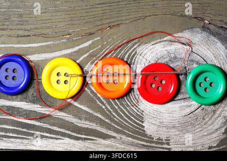 Several buttons of different types and a needle with thread on an old wooden table Stock Photo
