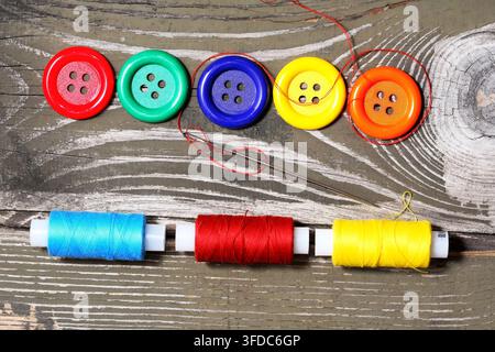 Several buttons of different types and a needle with thread on an old wooden table Stock Photo