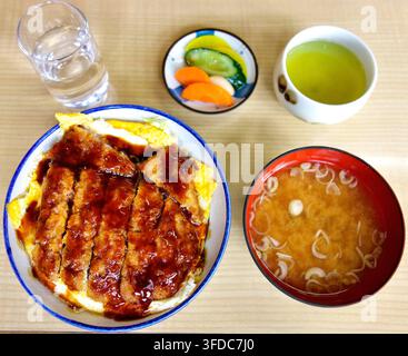 A delicious Japanese set meal featuring a pork cutlet rice bowl with sweet sauce and egg, served with miso soup, pickles, water, and green tea. Stock Photo