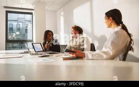 Business team meets in a bright white boardroom reviewing a laptop chart and notes during a calm morning strategy discussion Stock Photo