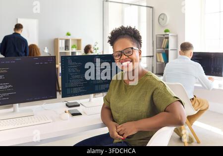 Happy woman programmer at computer workstation in bright office with code screens Stock Photo