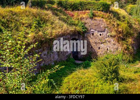 Remains of Maastricht fortifications with brick walls worn by time and covered in wild grass, abundant vegetation in background, sunny day in Frontenp Stock Photo